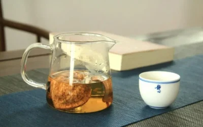 Aged Xinhui Chenpi citrus peel brewing in a glass teapot with a porcelain cup, showcasing a traditional Chinese tea drinking scene.