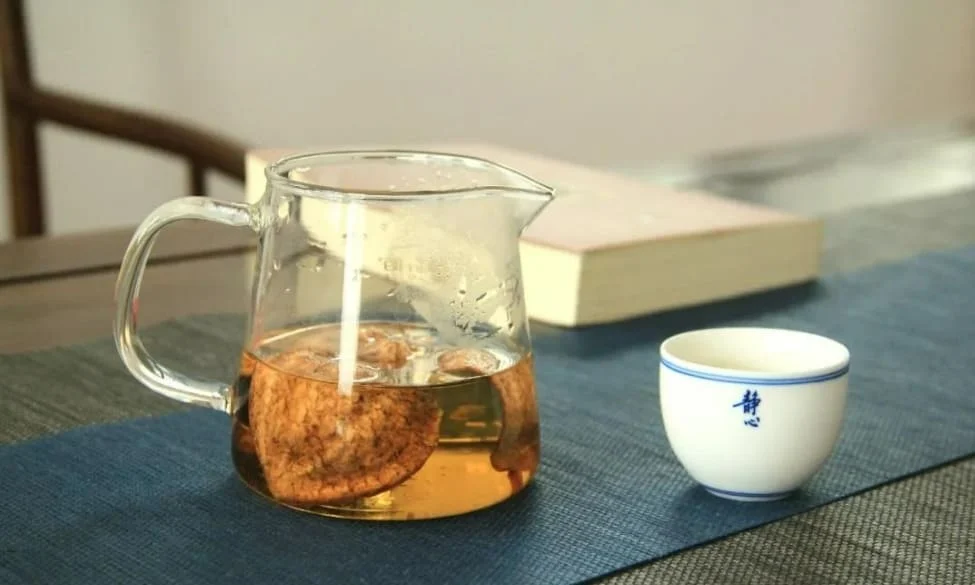 Aged Xinhui Chenpi citrus peel brewing in a glass teapot with a porcelain cup, showcasing a traditional Chinese tea drinking scene.
