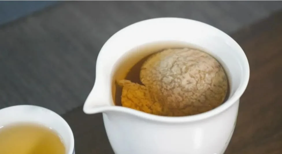 with aged Chenpi floating in a white porcelain cup, showing its golden amber color and rich citrus aroma.