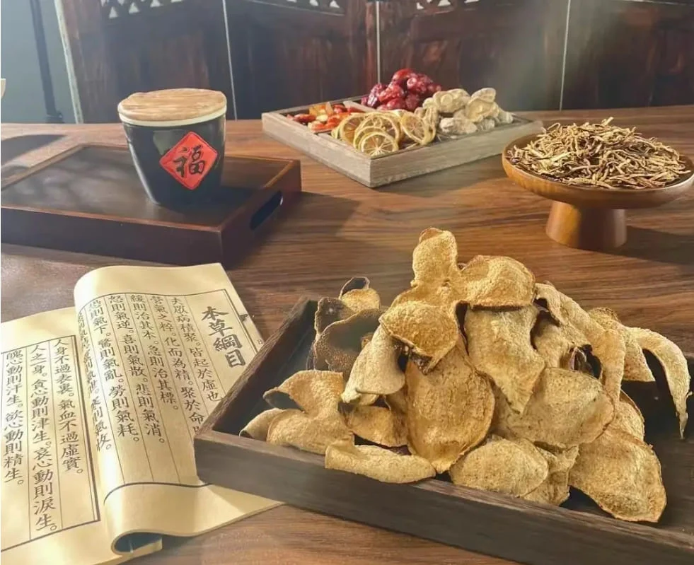 A traditional setup showing aged chenpi citrus peel, dried herbs, and a Chinese medical classic "Bencao Gangmu" used in traditional herbal tea practices. 