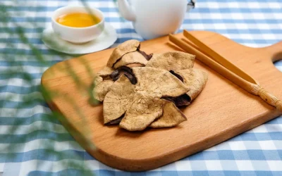 A lifestyle setting showing premium Xinhui Chenpi on a wooden board with bamboo tongs, accompanied by a white teapot and a cup of golden citrus tea, illustrating the traditional way to enjoy this healthy herbal drink.
