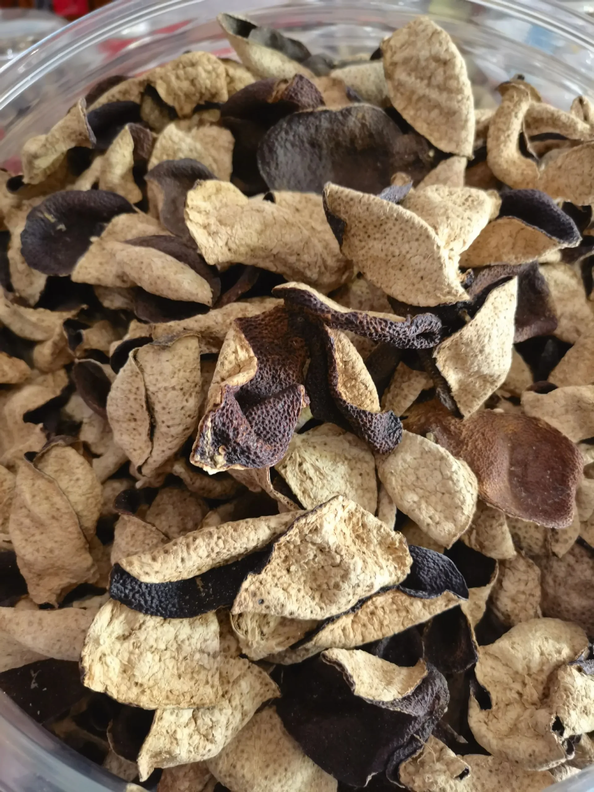 A detailed view of OuDaTea's high-quality Aged Chenpi (Dried Tangerine Peel) stored in a transparent container, highlighting the rustic, dried texture and rich color of the authentic Xinhui product.